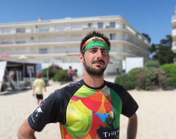 homme portant un bandeau vert et orange et un maillot coloré à la plage